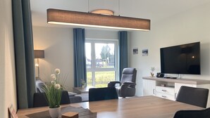 Un'area pranzo moderna con un tavolo in legno, sedie nere, una televisione e vista sull'esterno.