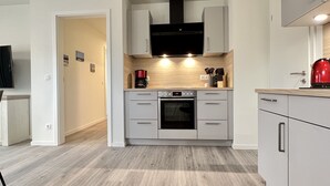 Una cucina moderna con mobili grigi, forno integrato e bollitore rosso sul piano di lavoro.