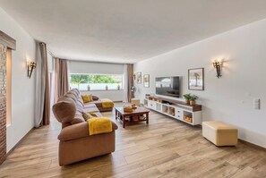 A modern living room with a sofa, TV, and wooden flooring. - Casa dos Netos - villa with private pool (São Bartolomeu de Messines)