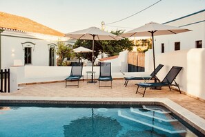 A pool area with lounge chairs and umbrellas, surrounded by a white building with a tiled roof. - Casa Dona Antonia - 6 bedrooms with private pool (São Bartolomeu de Messines)