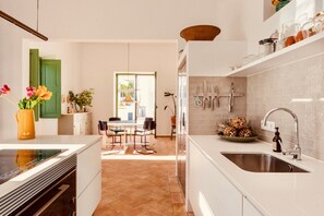 A modern kitchen with white cabinetry, a large island with a sink, and a dining area with a table and chairs. - Casa Dona Antonia - 6 bedrooms with private pool (São Bartolomeu de Messines)