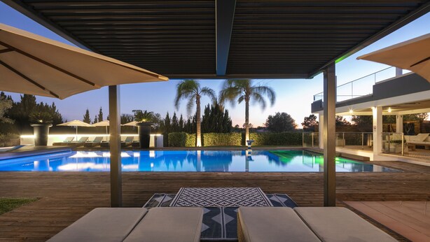 Ett område vid poolen med solstolar och parasoller, fri sikt över poolen och en modern arkitektonisk design.