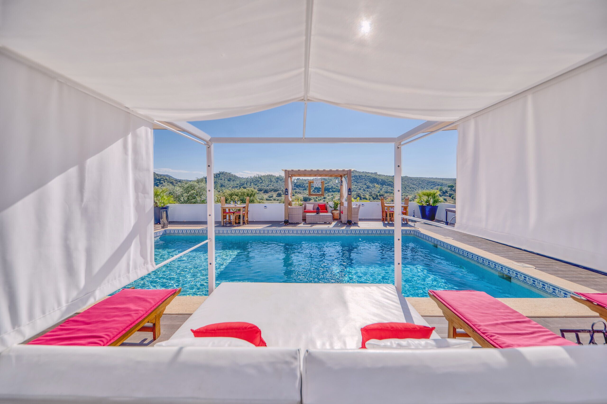 A pool area with white canopies, lounge chairs, and a view of a mountainous landscape.