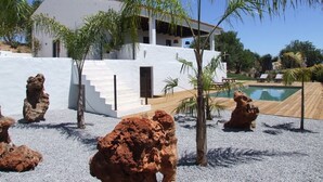 A white building with a pool, palm trees, and rock formations. - Casa Toia - amazing luxury farmhouse! (São Bartolomeu de Messines)