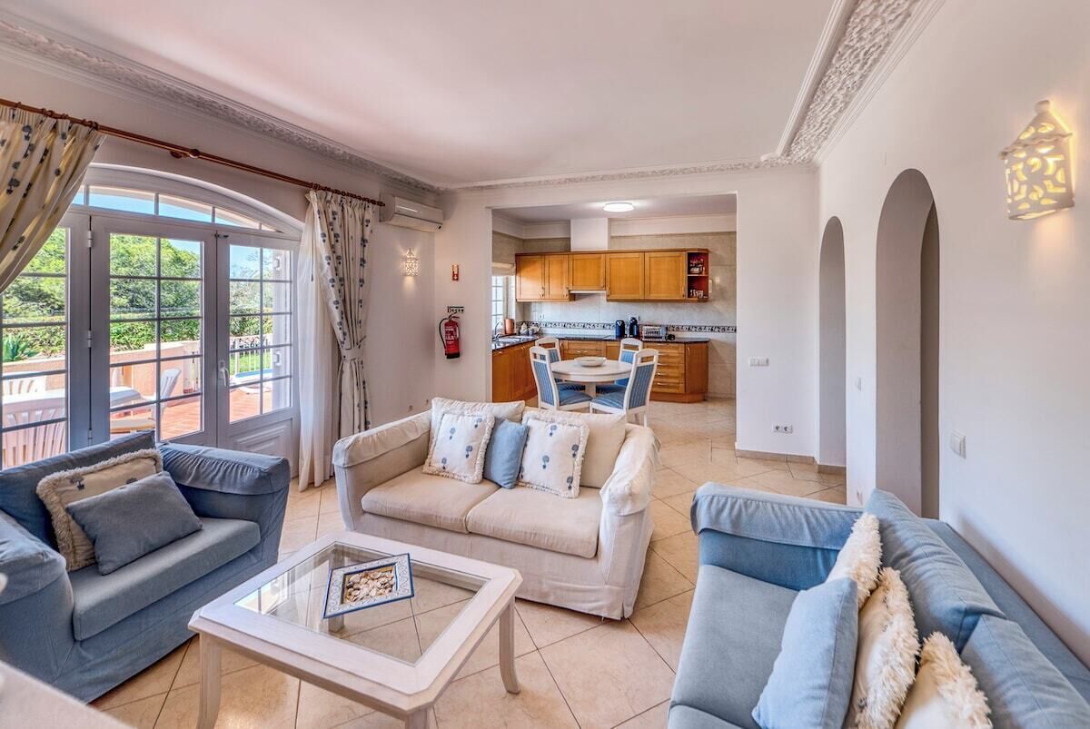 Ein Wohnzimmer mit einer Couch, einem Couchtisch und Blick auf die Küche und den Außenbereich.