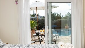 Une chambre avec un lit, une table avec des boissons, et une vue sur une piscine à travers une porte vitrée.