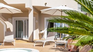 Un espace piscine avec des chaises longues et des parasols, un jacuzzi et des plantes en pot.