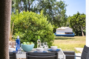 Un espace de restauration en plein air avec une table dressée pour deux personnes, entouré de verdure et avec un bâtiment en arrière-plan.