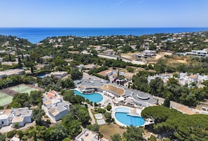 An aerial view of a coastal residential area with two swimming pools, a tennis court, and a variety of houses and buildings. - Casa Yaneliz - renovated apartment on nice resort! (Carvoeiro)