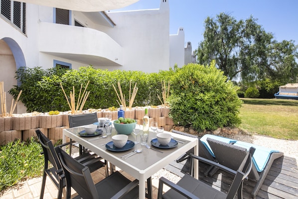 An outdoor dining area with a table set for four, surrounded by chairs and a wicker lounge chair. - Casa Yaneliz - renovated apartment on nice resort! (Carvoeiro)