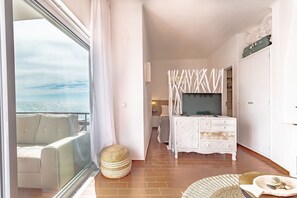 A balcony with a view of the sea, a white sofa, a wicker ottoman, and a white dresser with drawers. - Casa Seas - Stylish studio with amazing ocean view! (Carvoeiro)