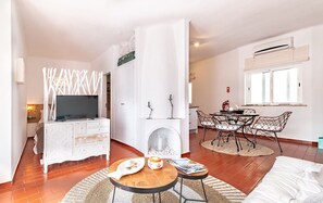 A modern living room with a TV, white furniture, a fireplace, and a dining area with chairs and a table. - Casa Seas - Stylish studio with amazing ocean view! (Carvoeiro)