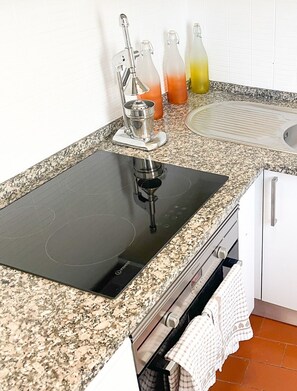 A kitchen with a black induction cooktop, a stainless steel sink, and a granite countertop. - Casa Seas - Stylish studio with amazing ocean view! (Carvoeiro)