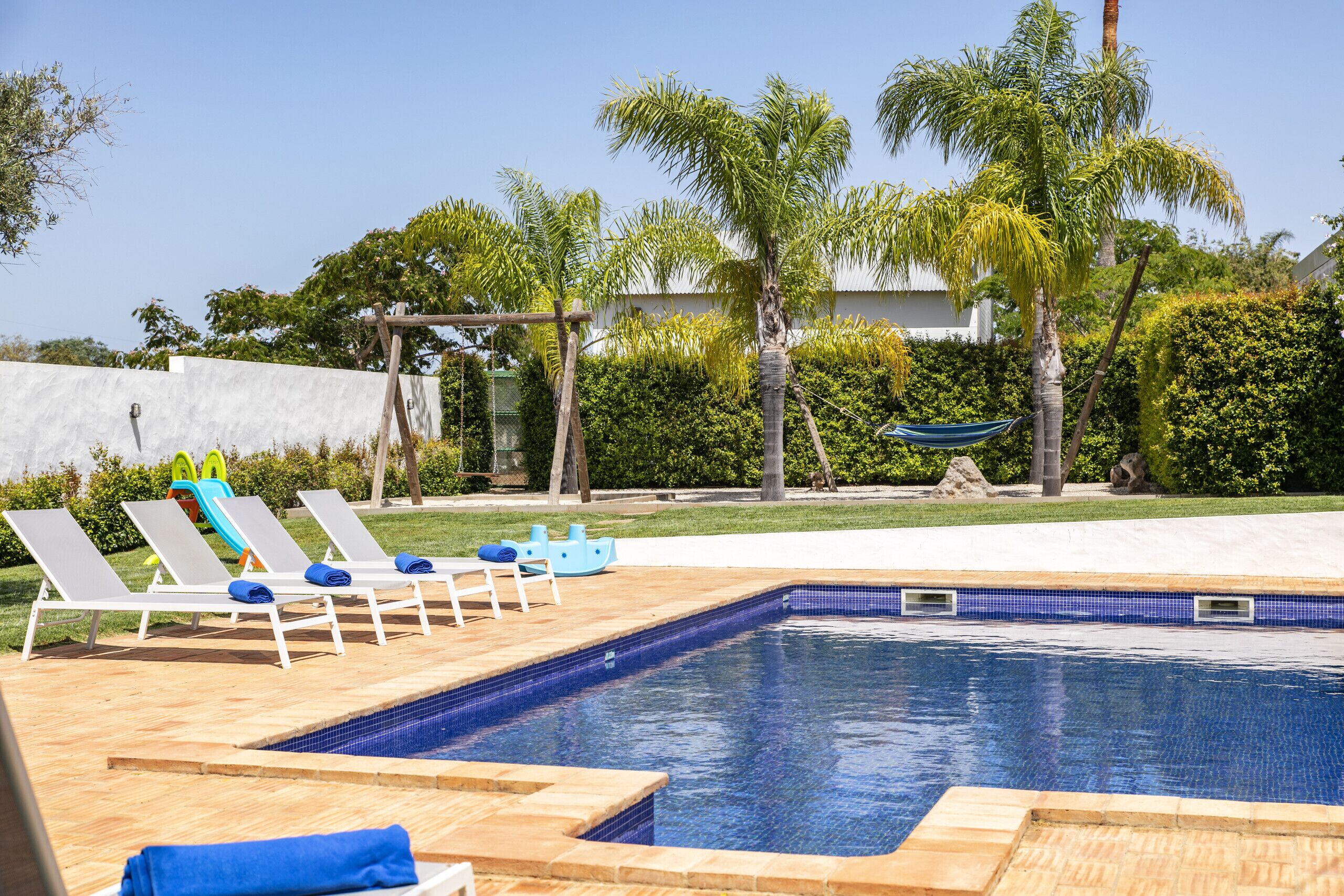 Una piscina con sillas de descanso, una hamaca y palmeras.