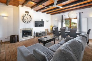 A living room with a fireplace, a large clock, a dining area with chairs, and a ceiling fan. - Casa Gloria - Lovely farm house with private pool! (Alcantarilha)