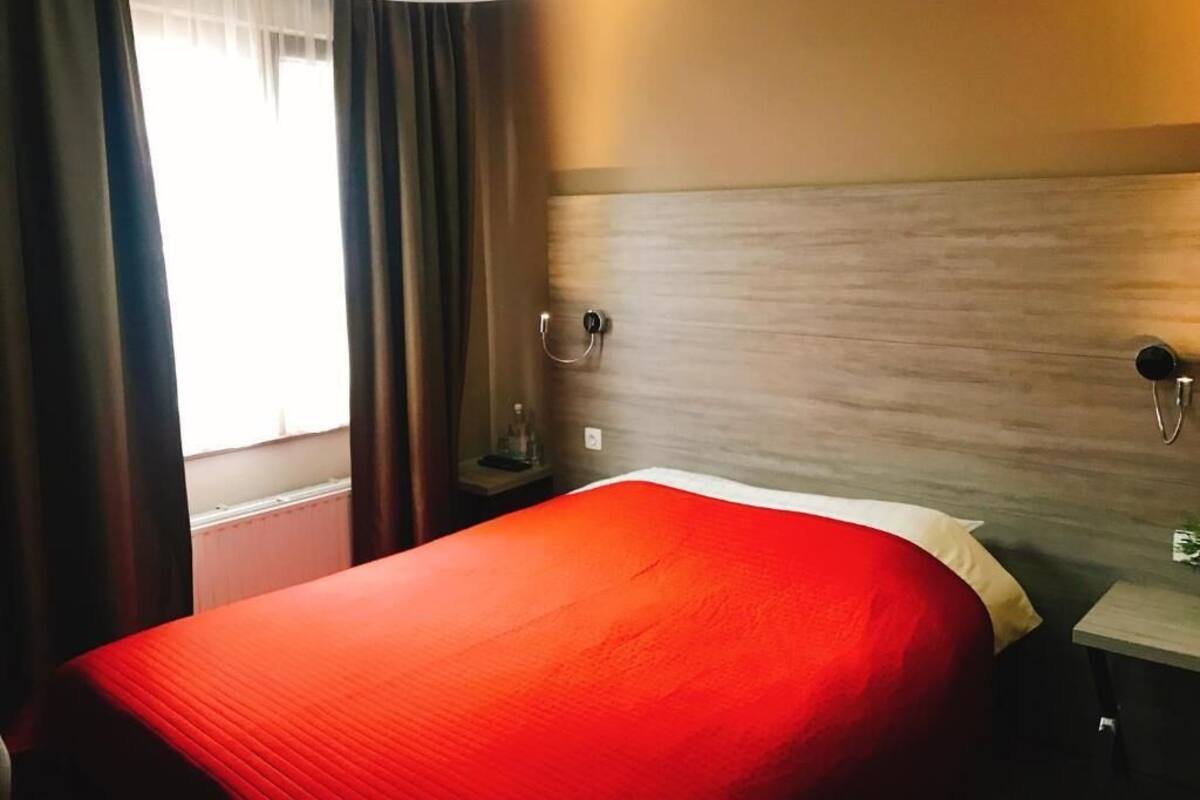 A hotel room with a bed, a nightstand, a lamp, and a window with curtains.