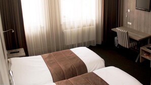 A hotel room with two beds, a TV, a desk, and a window with sheer curtains. - Hotel Mille Colonnes (Leuven)