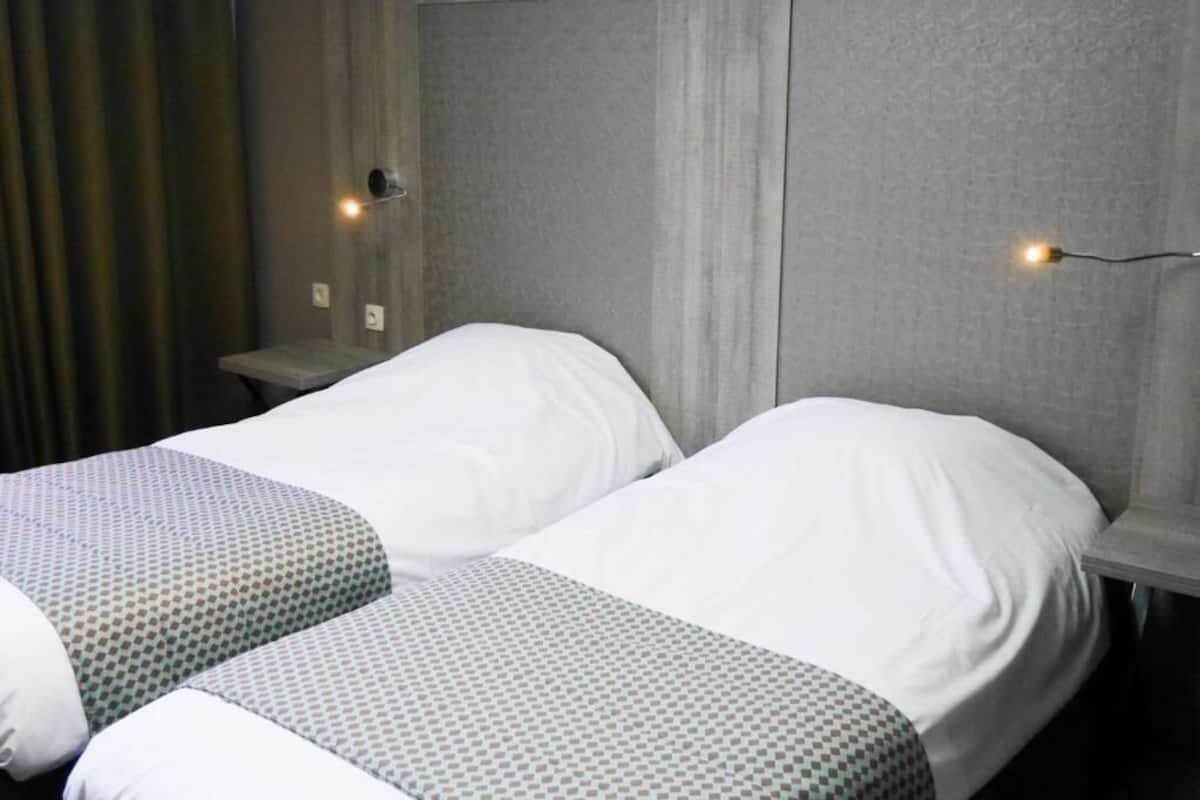 A hotel room with two single beds, grey headboards, and bedside lamps.