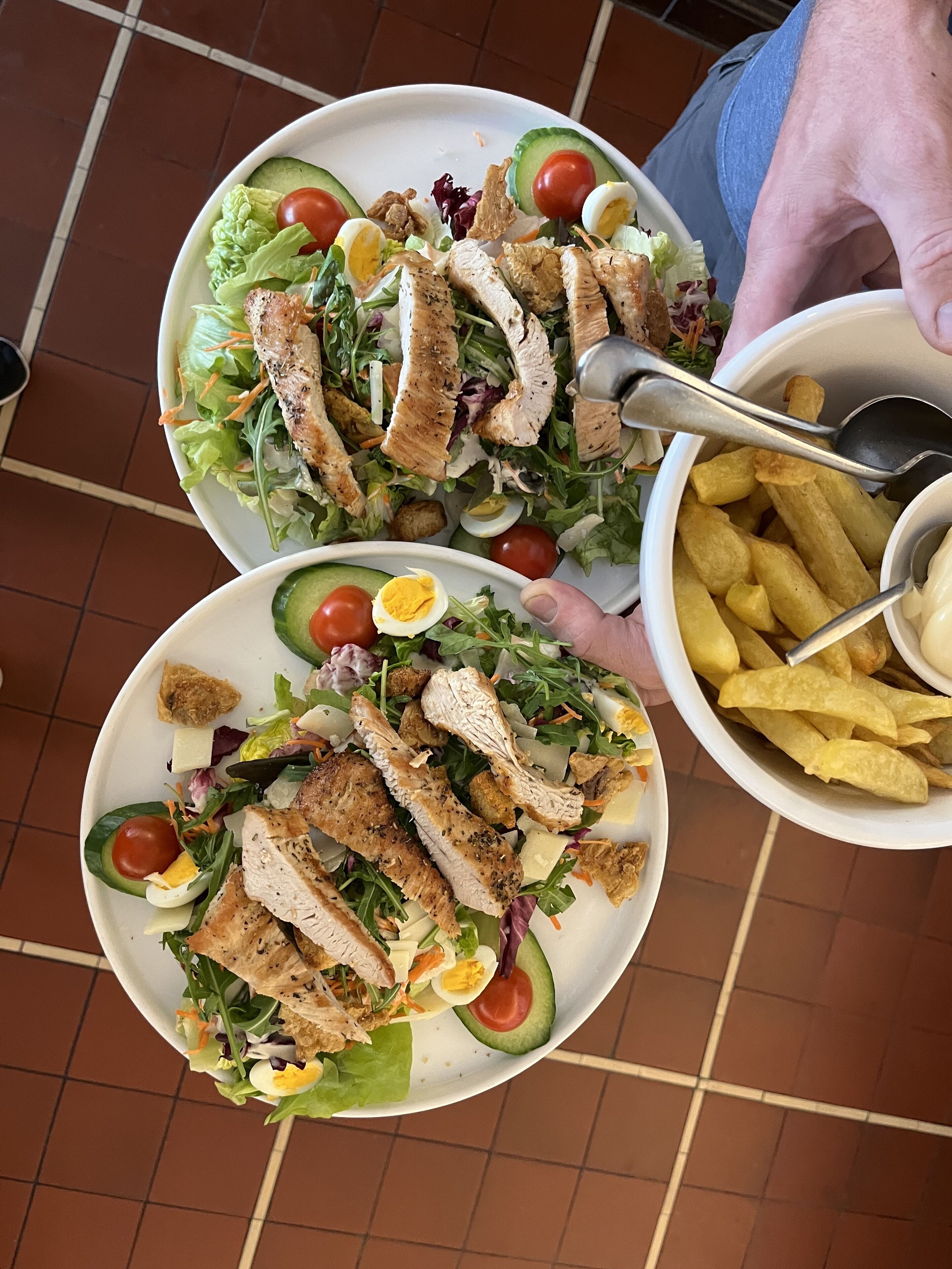 Een maaltijd bestaande uit een salade met kip, avocado en eieren, en een portie friet.