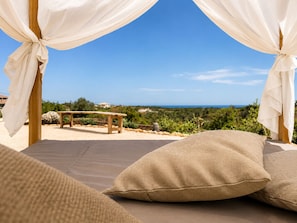 A bedroom with a view of the sea, a wooden bench, and a table in the background.