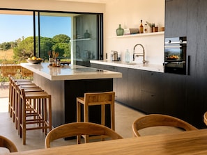 A modern kitchen with a large island, bar stools, and a view of greenery outside. - Casa Mú | Luxury Villa & Private Pool (Lagoa)