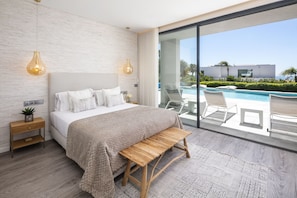 A modern bedroom with a large bed, bedside tables, a bench, and a view of a swimming pool. - Villa da Raposa - Stunning ocean view villa! (Lagos)