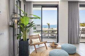 Una sala de estar moderna con un ventanal grande, un sillón de mimbre, una planta en maceta y vistas al mar.