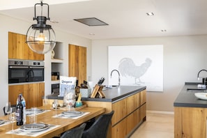A modern kitchen with wooden cabinets, a central island, and a dining area set for six. - Villa da Raposa - Stunning ocean view villa! (Lagos)