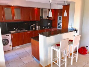 A modern kitchen with wooden cabinets, a built-in oven, and a central island with bar stools. - Casa Vale - apartment with pool on golf resort (Lagoa)