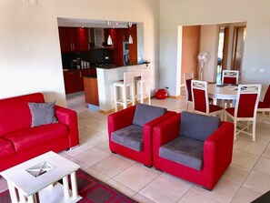 A modern living room with red sofas, a dining area with white chairs, and a kitchen in the background. - Casa Vale - apartment with pool on golf resort (Lagoa)