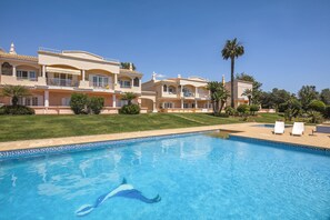 Ein Pool mit Delphin-Motiv, umgeben von gepflegtem Rasen und Palmen.