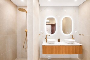 A modern bathroom with a walk-in shower, two sinks, and a wooden vanity.