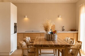 A modern kitchen with a wooden dining table, white cabinets, and a vase with dried flowers.