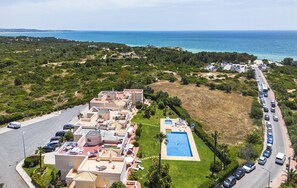 Luftaufnahme eines Küstenresorts mit Villen, einem Schwimmbad und einer Straße mit geparkten Autos.