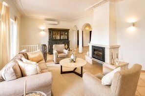A living room with a fireplace, beige sofas, a coffee table, and a dark wooden cabinet.
