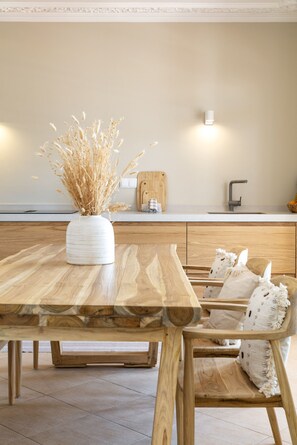 Ein Holztisch mit einer Vase getrockneter Blumen, Holzstühle, eine Küchenarbeitsplatte und eine Leuchte.