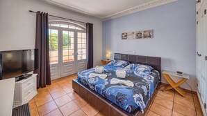 A bedroom with a bed, a TV, a desk, and a window with curtains.