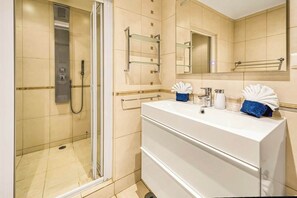 A modern bathroom with a glass-enclosed shower, a white vanity with a mirror, and a towel rack.