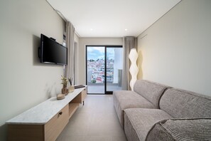 A modern living room with a flat-screen TV, a sofa, a console table with decorative items, and a view of a cityscape through a glass door. - The Beach House Carvoeiro - Cliffside Apartment (Carvoeiro)