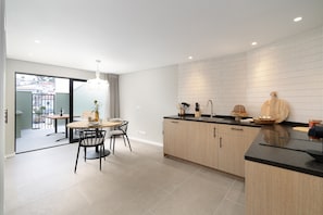 A modern kitchen with a dining area, featuring a large island, wooden cabinets, and a tiled backsplash. - The Beach House Carvoeiro - Cliffside Apartment (Carvoeiro)