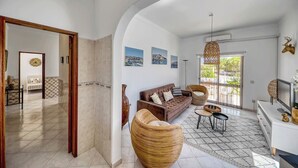 Ein geräumiger Wohnbereich mit einer Couch, Korbstühlen, einem Fernseher und Kunstwerken an der Wand.