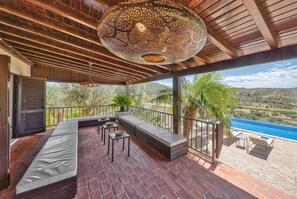 A covered outdoor seating area with a view of a swimming pool and hills. - Villa Fuzeiros - Amazing villa in a green valley! (São Bartolomeu de Messines)
