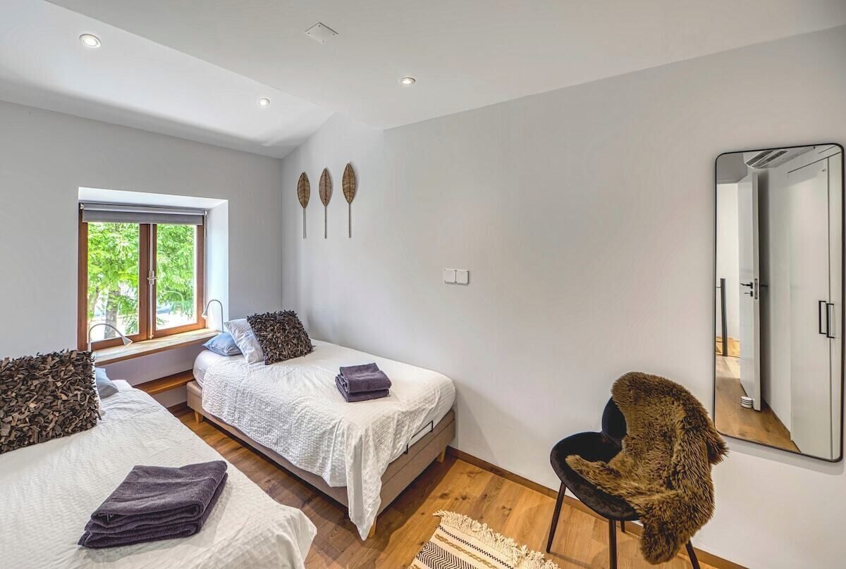 A modern bedroom with two beds, a large window, a mirror, and a unique furry chair.