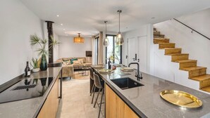 Une cuisine moderne dotée d’un îlot central, d’un four encastré et d’un escalier en bois.