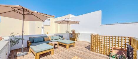 A wooden deck with a sofa and two umbrellas, a wooden table, and a wooden fence.