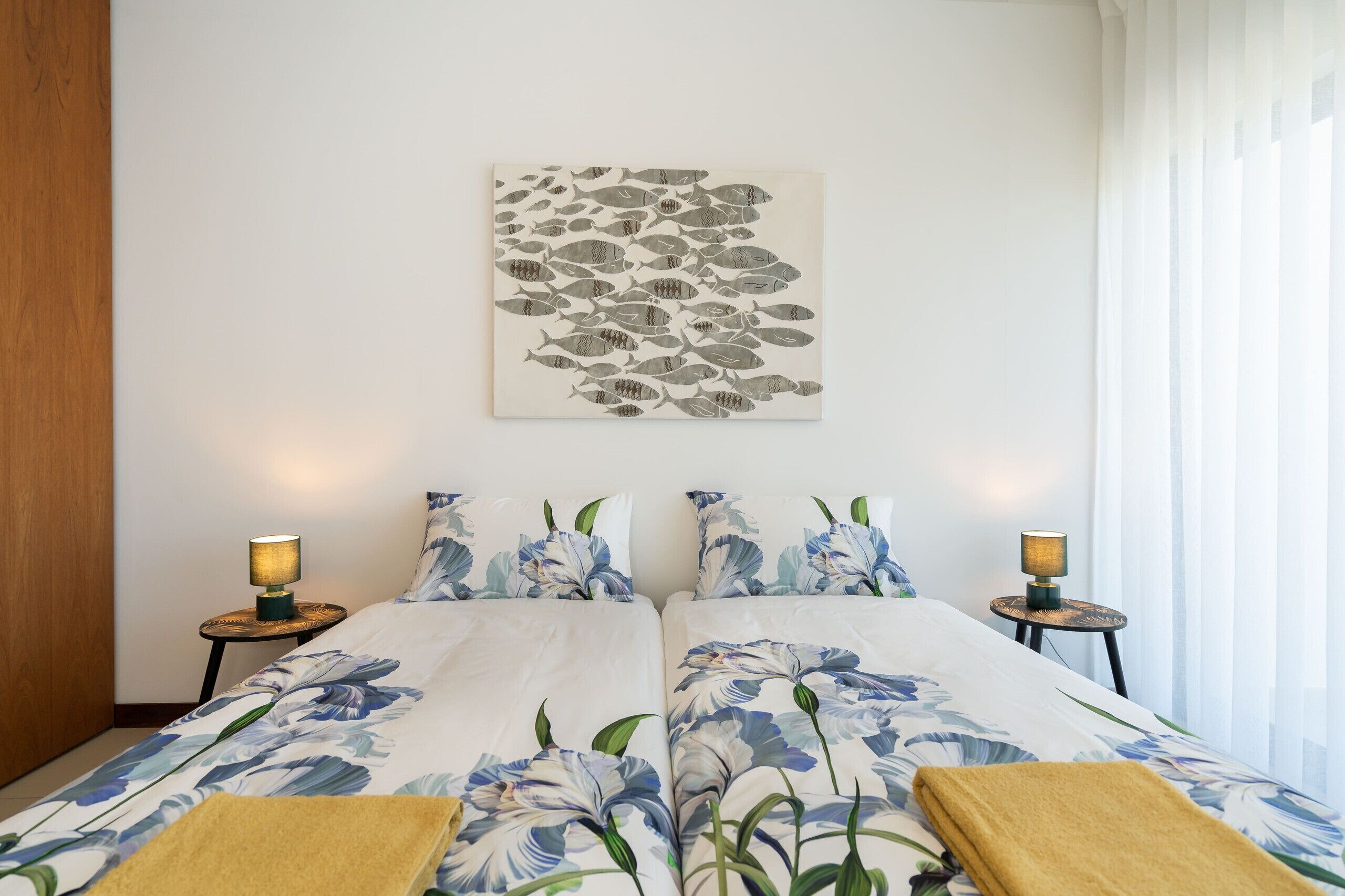A hotel room with a bed, two bedside tables with lamps, a floral bedspread, and a wall-mounted artwork of fish.