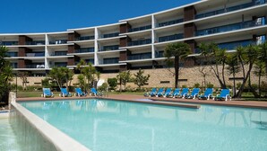 Un hotel moderno con zona de piscina, varios balcones y sillones de descanso.
