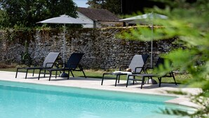 A swimming pool with lounge chairs and umbrellas, surrounded by a stone wall and greenery. - Studio Michel (Pichanges)