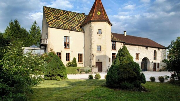 A historic building with a prominent tower and a patterned roof, surrounded by well-maintained gardens. - Studio Michel (Pichanges)