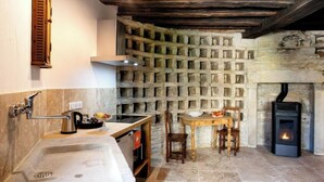 A rustic kitchen with a stone wall, a wooden table, and a fireplace. - Studio Michel (Pichanges)